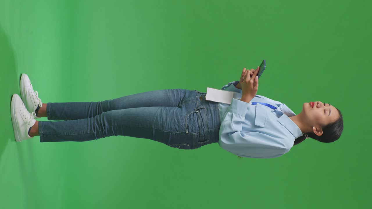 휴대 전화를 사용하는 아시아 사업가 여성의 전체 몸의 측면 뷰 스튜디오의 녹색 화면 배경에서 주변을 둘러보고