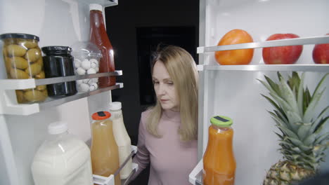 Late-at-night,-a-woman-looks-inside-a-large-refrigerator.-Night-snack-concept