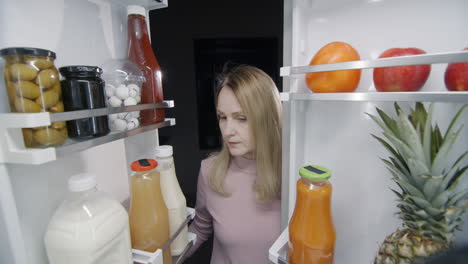 tarde en la noche, una mujer mira dentro de un gran refrigerador. concepto de bocadillo de noche