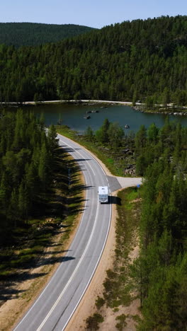 aerial: camper driving in middle of forest and lakes, summer in inari, lapland