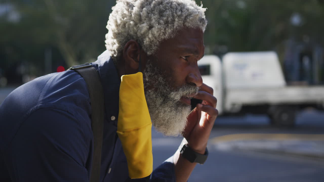 Nahaufnahme eines afroamerikanischen Seniors mit Gesichtsmaske, der auf der Straße mit dem Smartphone telefoniert.