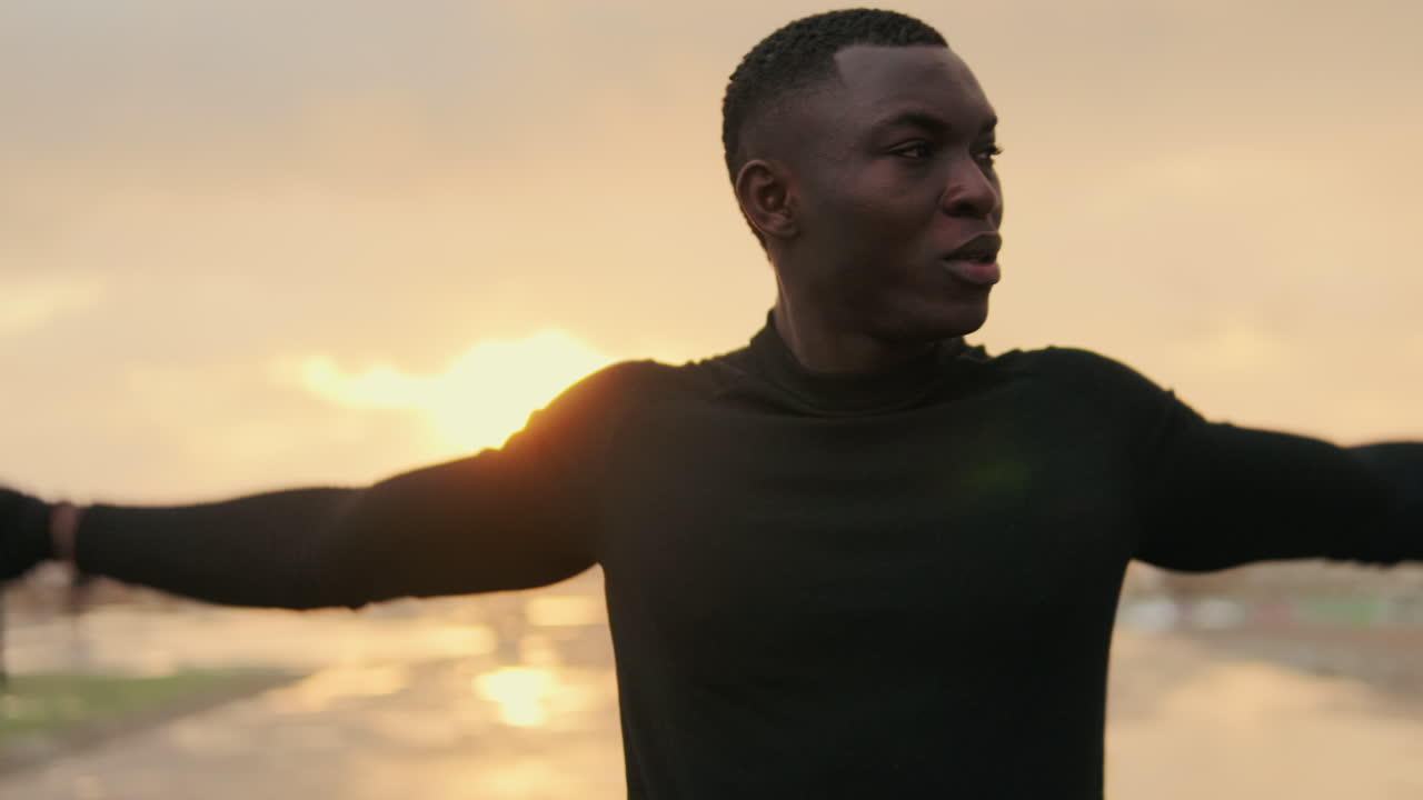 Joven negro estirando los brazos al aire libre durante un atardecer dorado.