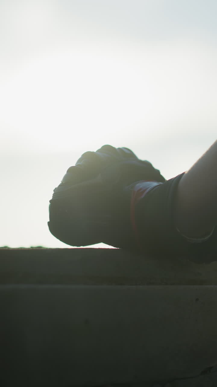 vista trasera de un individuo en una camisa a cuadros con un guante de protección, con la mano sujetada en un puño descansando en una cornisa de la ventana