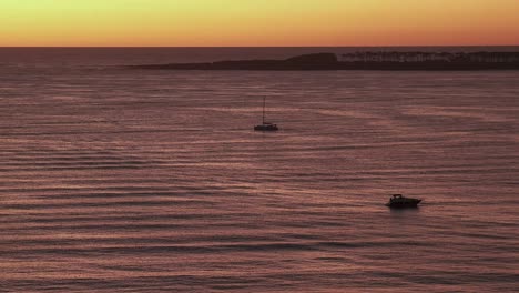 time lapse shot of sailing boat cruising on sea during golden sunset at horizon - aerial wide shot