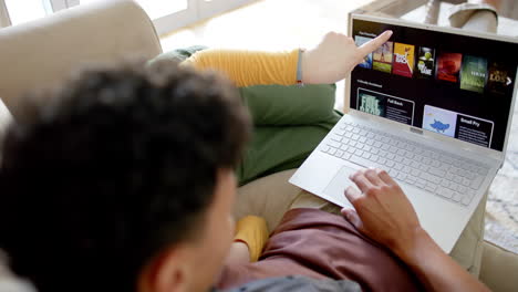 una pareja feliz sentada en el sofá usando una computadora portátil en casa, en cámara lenta