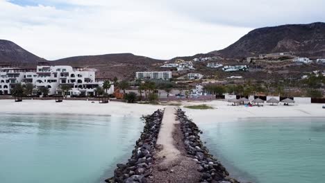 Aerial-dolly-shot-off-the-coast-of-Playa-El-Caymancito-near-La-paz-Baja-California-Sur-Mexico-on-the-beach-with-view-of-hotel-building,-dry-landscape-and-the-blue-sea