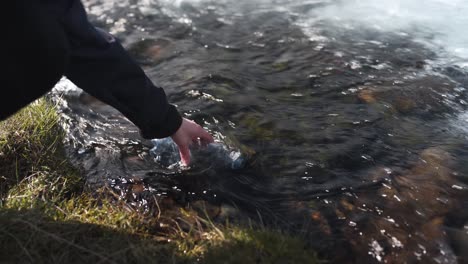 closeup of a female hand filling up a plastic bottle with fresh glacier water coming from the waterfall bruarfoss in iceland-1