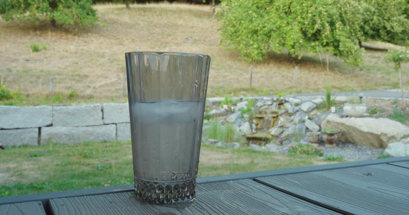 Copo de água gelada com uma nascente natural ao fundo. Ideal para conceitos de hidratação, água potável fresca, natureza e verão.