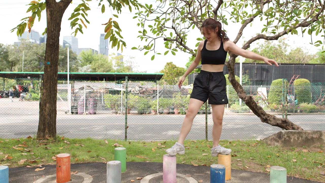 Una mujer en forma con ropa deportiva negra practica el equilibrio en postes de colores en un parque al aire libre