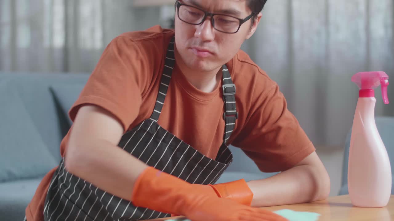 집에서 스프레이로 테이블을 청소하는 아프론을 입은 분노한 아시아 남성 집무원