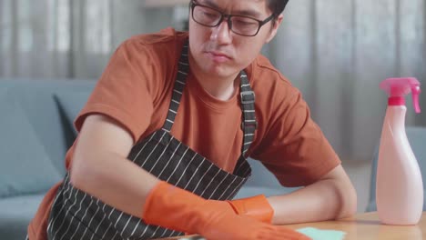 close up of angry asian male housekeeper with an apron cleaning the table by the spray at home