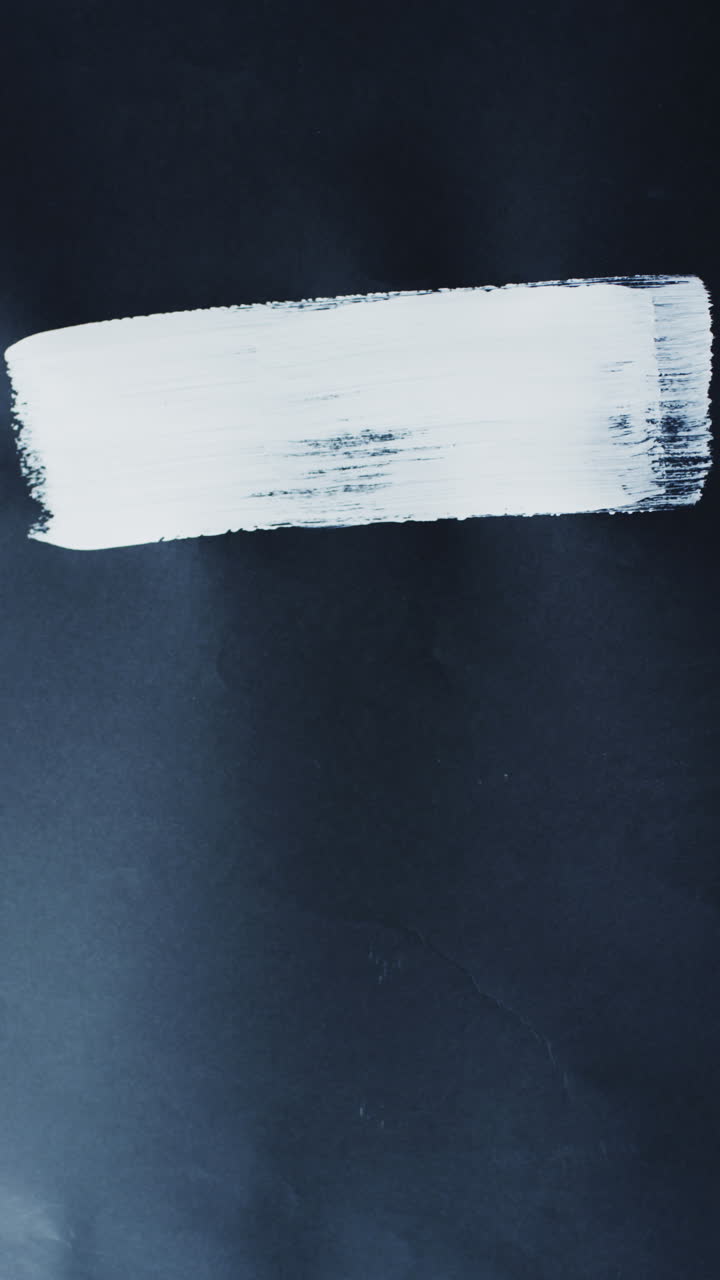 Vertical video of white paint stripe on black background with copy space, slow motion