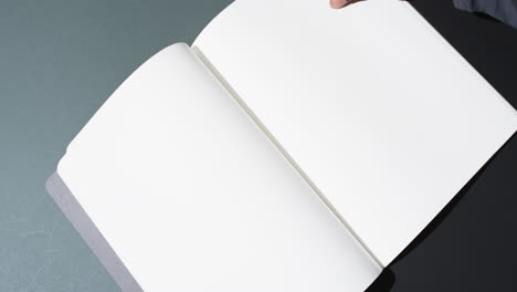 Video-of-hand-of-african-american-man-holding-book-with-blank-pages,-copy-space-on-black-background