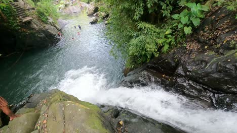 Adult-person-at-Kroya-Waterfall-sliding-down-rocks-of-vertical-natural-waterslide-amid-lush-tropical-forest-of-Aling-Aling-falls,-Bali