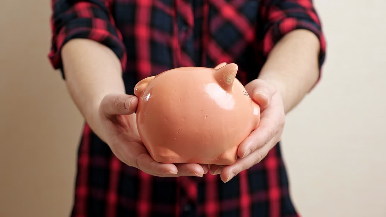 여자 는 작은 둥근 돼지 은행 을 들고 은 팔 을 펴고 있다