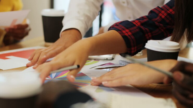 Close-up view of hands of multiethnic people pointing graphics and using calculator on smartphone on a table in a cafe