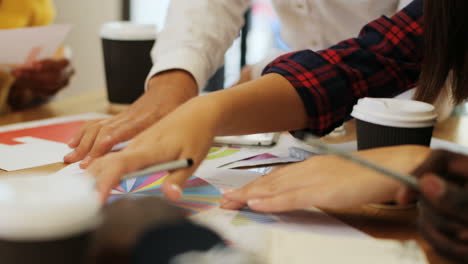 close-up view of hands of multiethnic people pointing graphics and using calculator on smartphone on a table in a cafe