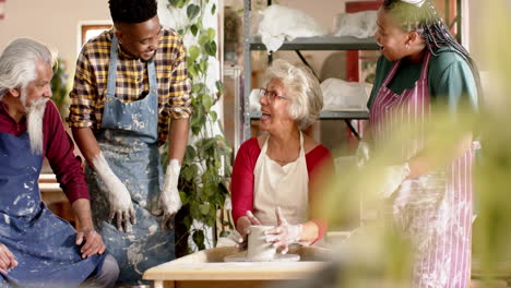 Happy-biracial-female-potter-with-others,-using-potter's-wheel-in-pottery-studio,-slow-motion