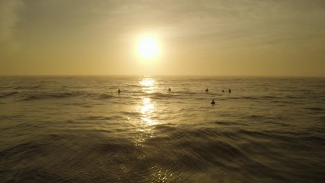 Stunning-sunrise-aerial-with-silhouette-of-surfers-on-calm-waves-in-Pacific-ocean