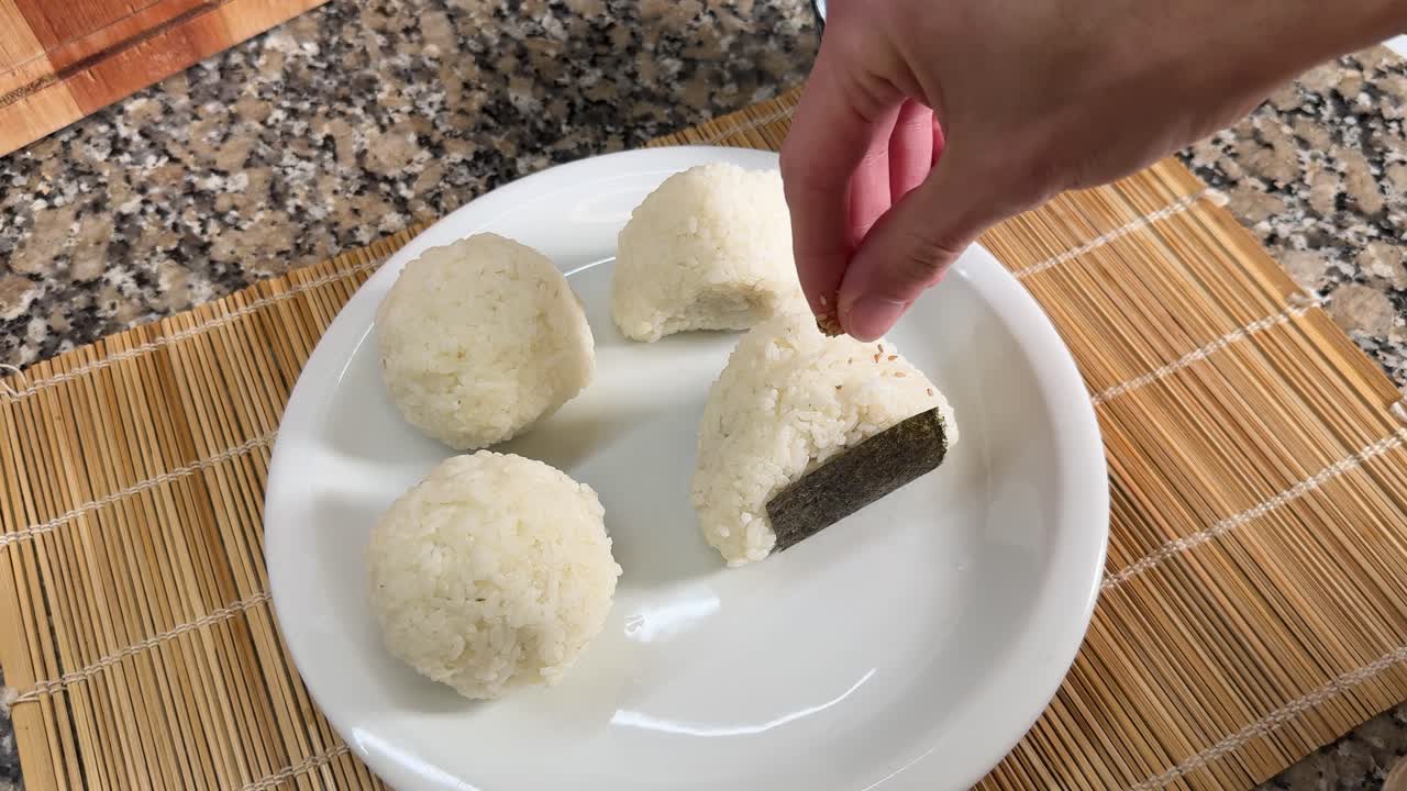 A Hand is Sprinkling Sesame Seeds on Top of Onigiri - Close Up
