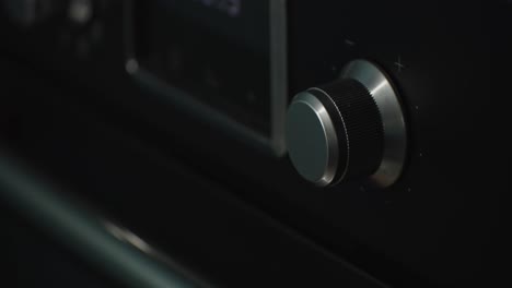 person turning up temperature knob of black oven in home kitchen, close up