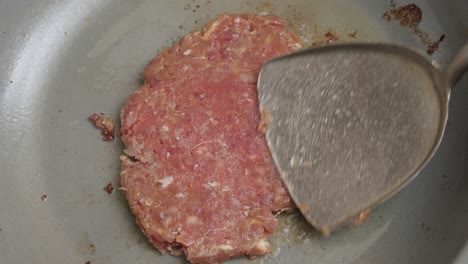 cooking and smashing with a spatula a burger patty in the frying pan