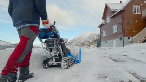 Man-clearing-snow-with-a-snow-blower-in-the-driveway-after-the-plow-moved-all-snow-back-on-private-property,-nice-mountains-in-the-background