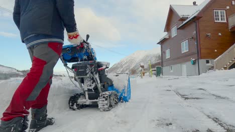 man clearing snow with a snow blower in the driveway after the plow moved all snow back on private property, nice mountains in the background