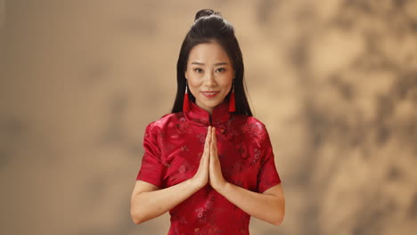 Portrait-of-young-Asian-woman-in-red-traditional-clothes-smiling-cheerfully-at-camera-and-doing-greeting-gesture