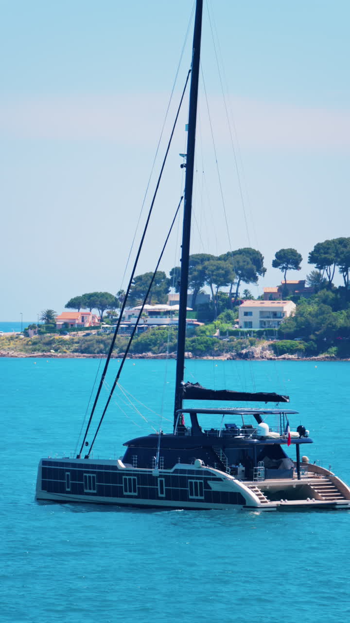 Boat floating on the Mediterranean sea with villas surrounded by greenery in the background. Vertical