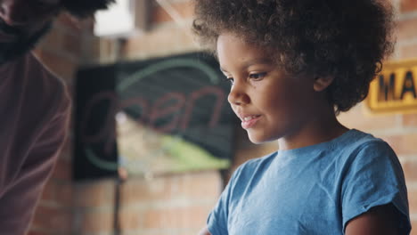 Pre-teen-mixed-race-boy-teen-standing-at-a-workbench-in-the-garage-building-a-racing-kart-with-his-dad,-low-angle,-close-up,-selective-focus,-focus-on-son