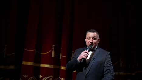 actor with microphone announces performance before auditorium. theater curtains background.