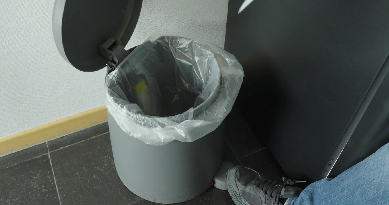 Person throwing a sheet of paper into a trash bin, representing document disposal, office cleanup, and waste management.