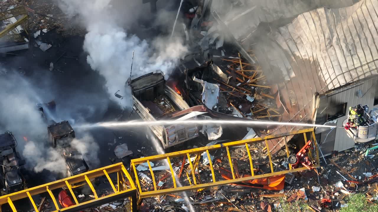 воздушный сверху вниз пожарный распыляет воду шлангом на горящие транспортные средства после взрыва газа - панорамный выстрел