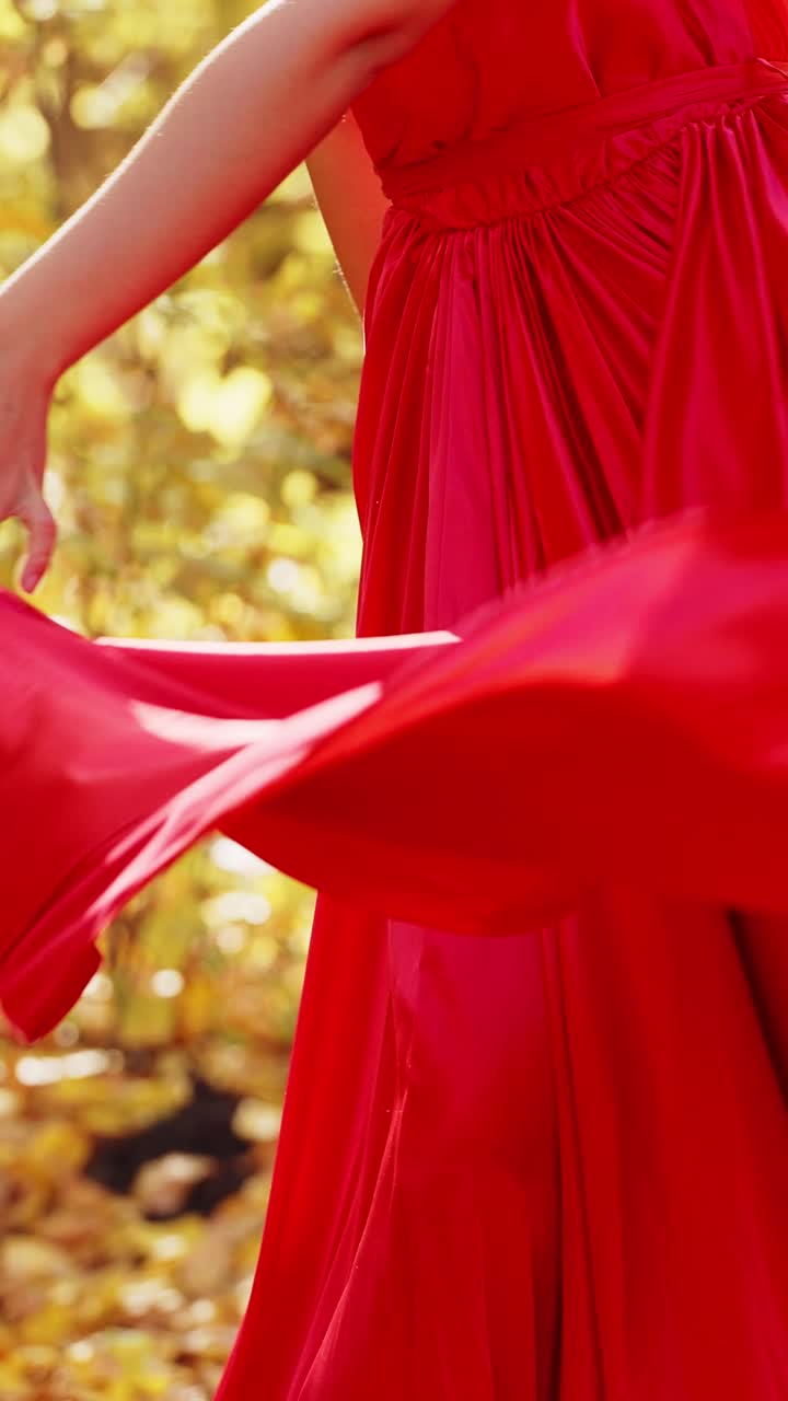 A Graceful Young Woman in a Flowing Red Dress Enjoys a Bright Autumn Day, Radiating Joy and Confidence Amidst Nature's Beautiful Golden Backdrop