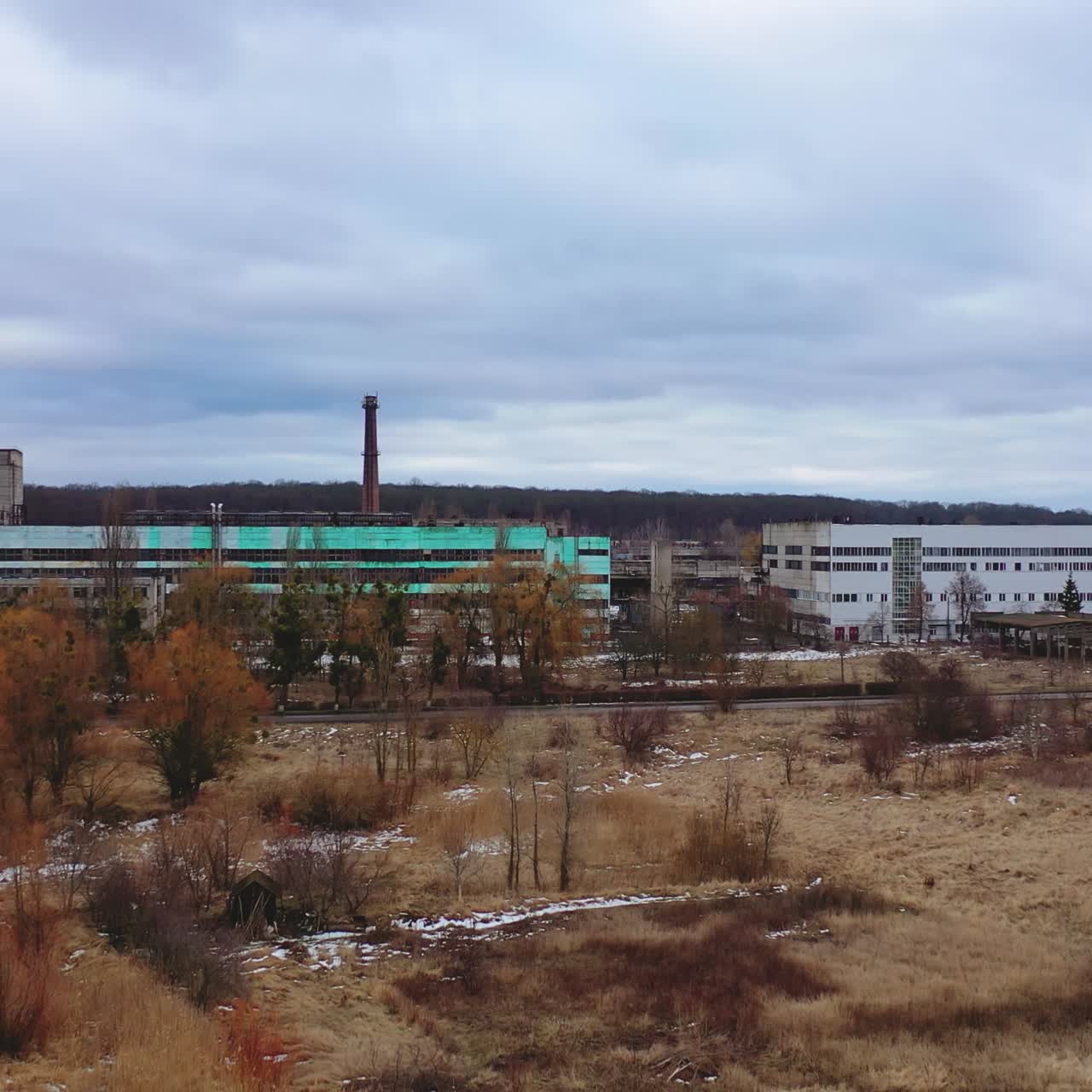 Old ruined factory among nature. Front view of a large ruined buildings of abandoned plant under gray sky