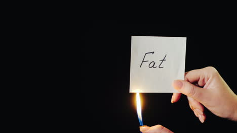 man burns a paper with the inscription fat