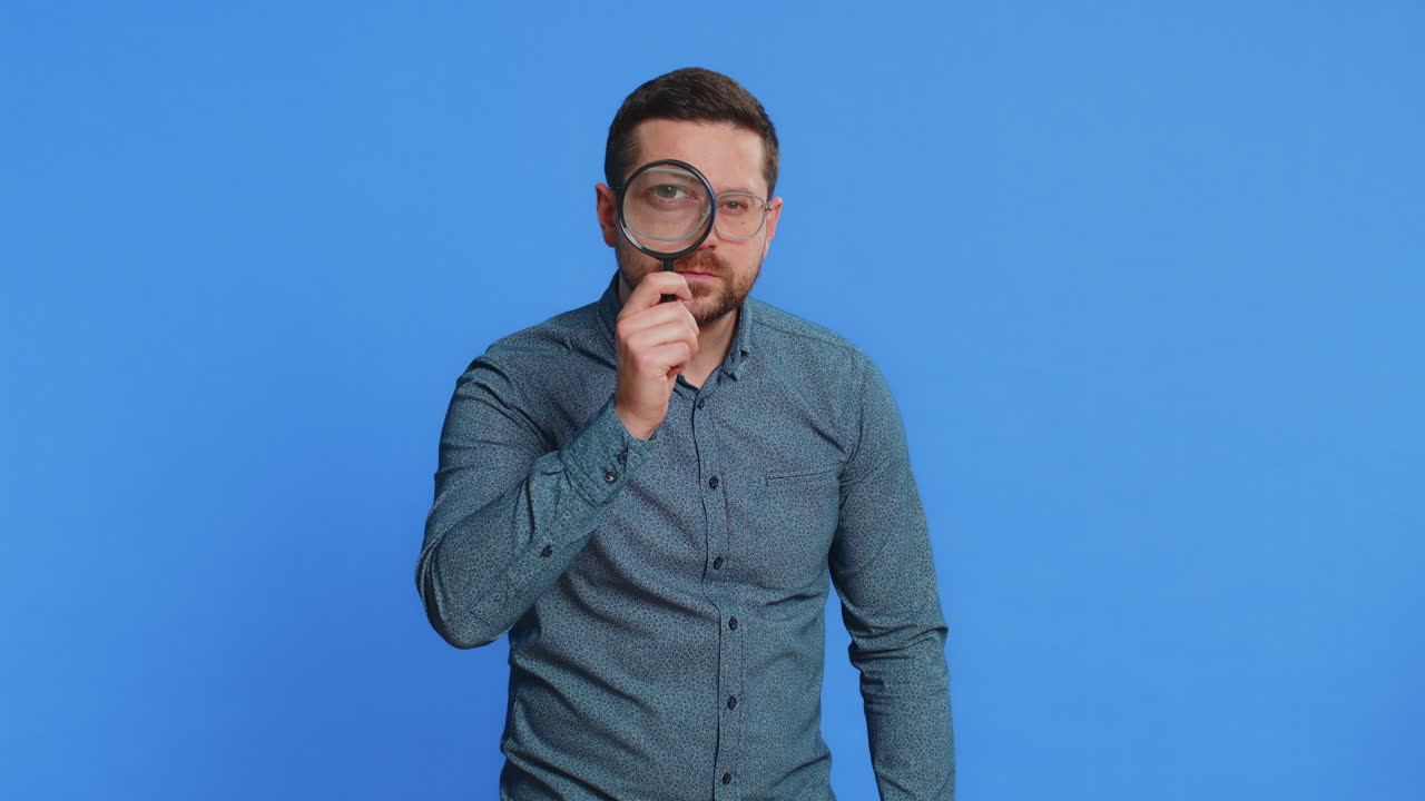 Middleaged man holds magnifying glass near face looking at camera with big zoomed eye analyzing
