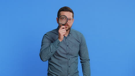 middleaged man holds magnifying glass near face looking at camera with big zoomed eye analyzing