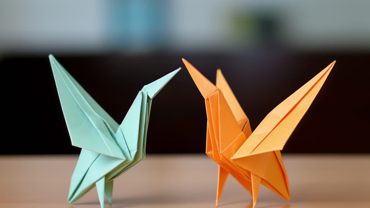 Origami paper birdsorange and light blueperching side by side, delicately positioned on wooden surface, representing precise folding technique and artistic expression