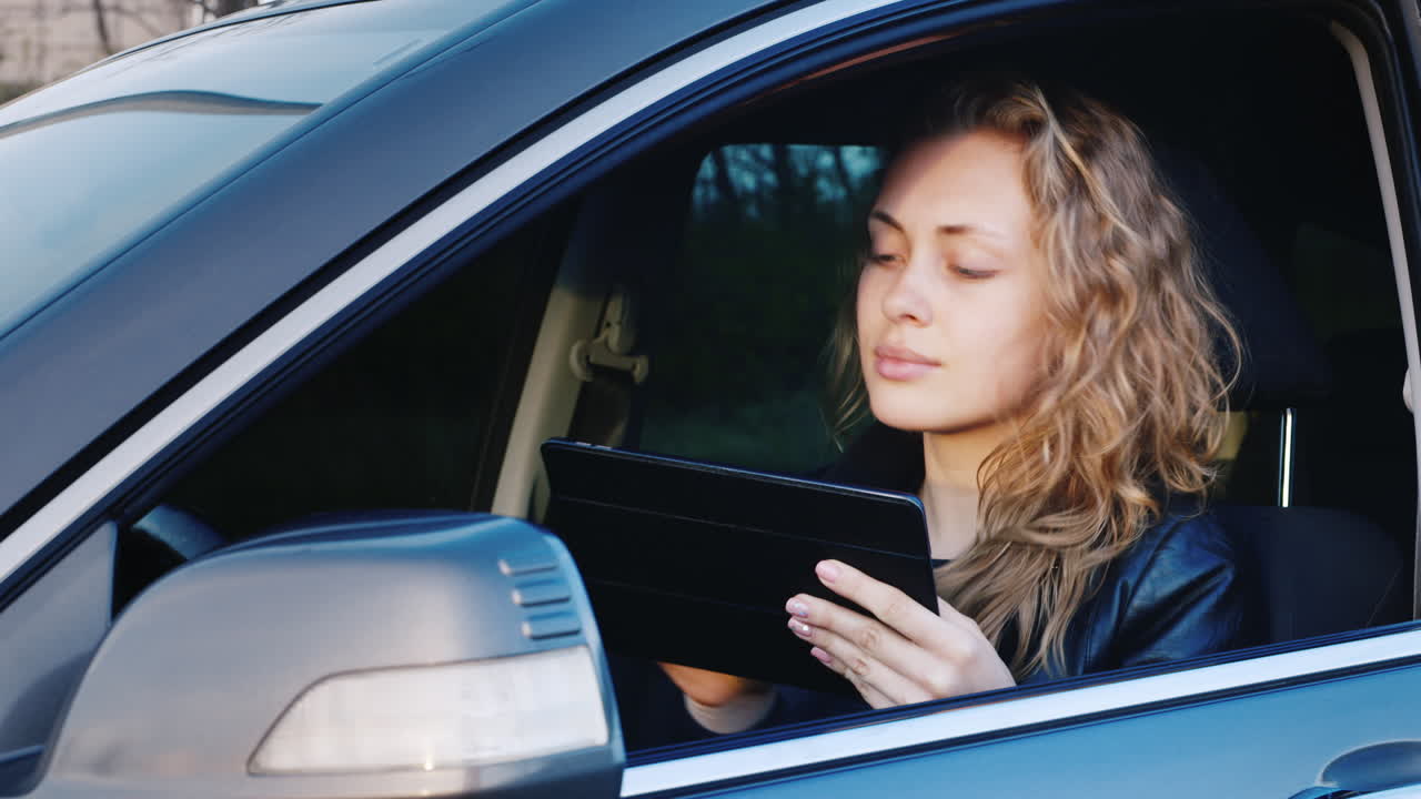 слегка встревоженная женщина пользуется планшетом, сидя за рулем автомобиля