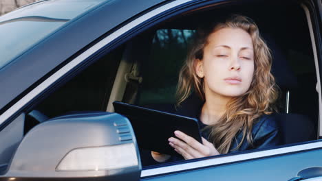 slightly alarmed woman uses a tablet while sitting at the wheel of the car