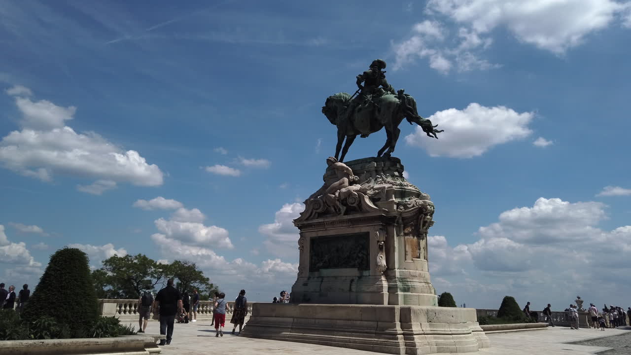 4K Statue of Prince Eugene of Savoy. The statue is at the centre of the scene. A blue sky full white clouds are in the background. People walk and take pictures around the statue.