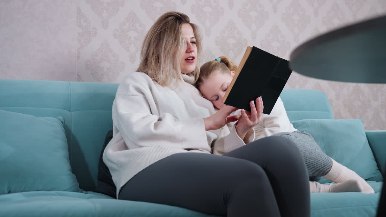 Mother reading book with daughter resting on shoulder, both sitting on sofa, sharing peaceful bonding moment with warmth, love, and education in cozy home environment filled with affection, comfort