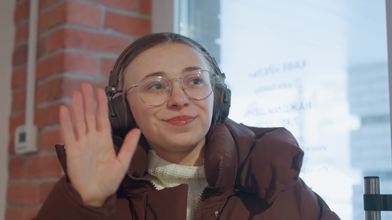 Giovane donna in cappotto invernale che si scalda le mani e saluta.