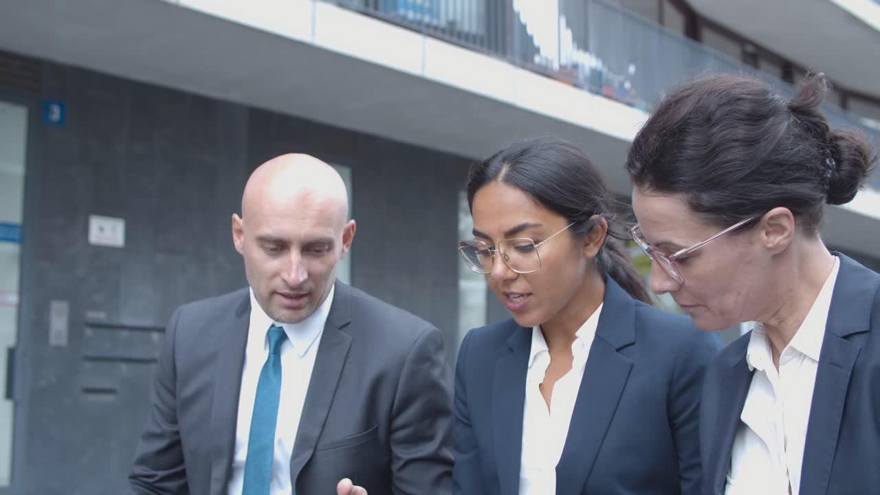 socios comerciales sentados juntos cerca del edificio de oficinas, hablando, viendo y discutiendo contenido en la computadora portátil