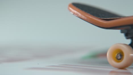 una toma hiper macro detallada de un mini patineta, pequeñas ruedas blancas, montar fingerboard de derecha a izquierda, iluminación profesional, estático cine 4k video