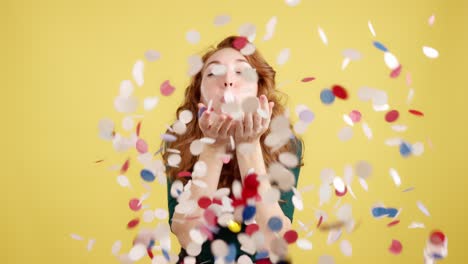 joyful woman blowing confetti against a yellow background