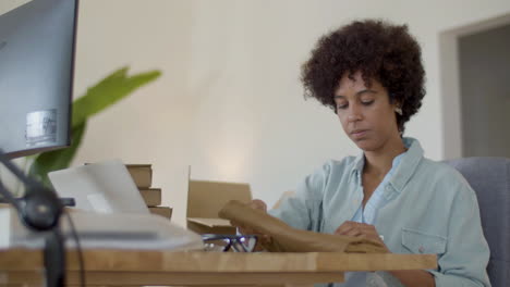 mujer negra seria comprobando la calidad de la ropa y poniendo dentro de la caja para enviar