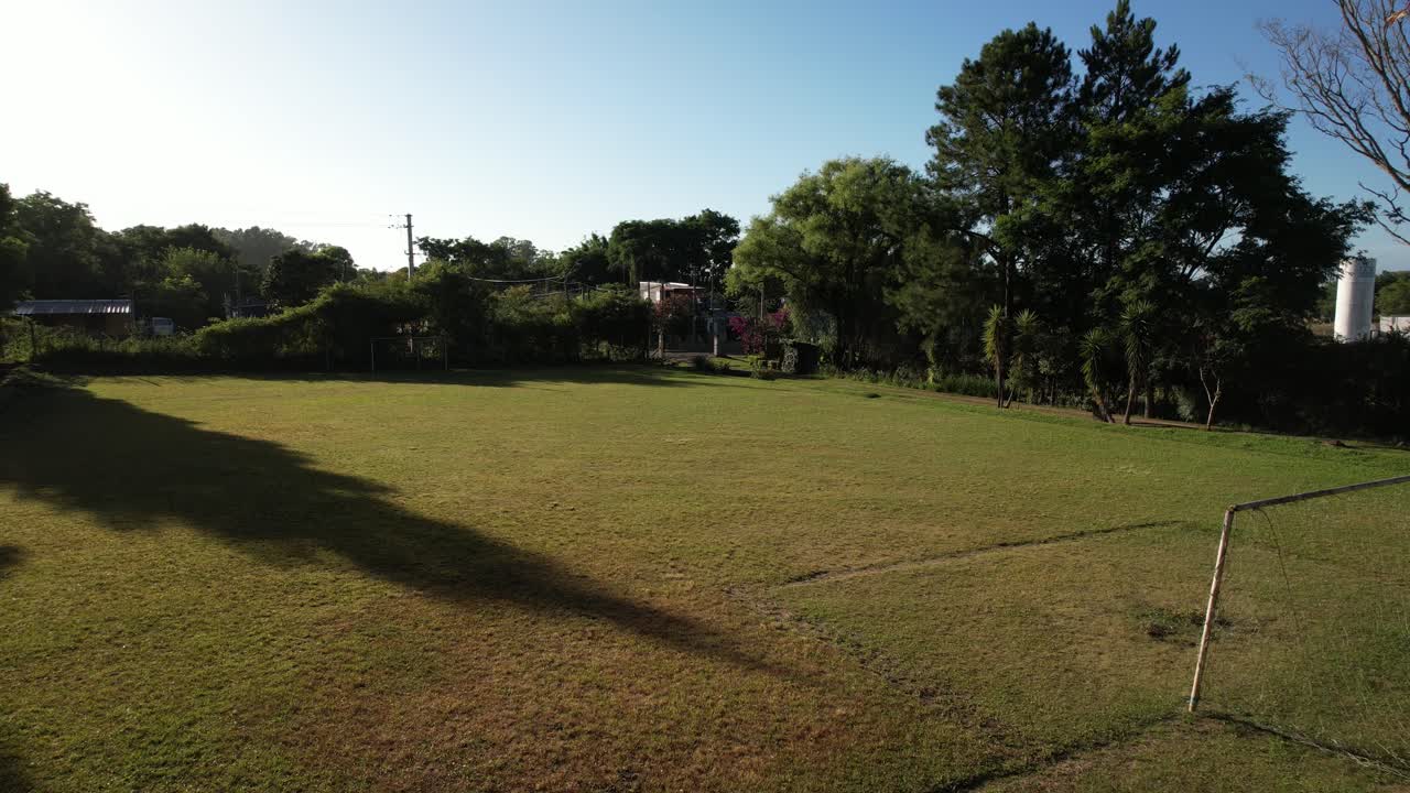 drone leaving a football field and crossing a landscape with many trees